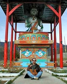 Craig Chaquico seated beneath 40 ft Tibetan Buddha statue at monastery